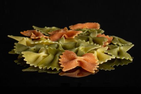 Lot of whole red, yellow and green uncooked farfalle isolated on black glassの写真素材