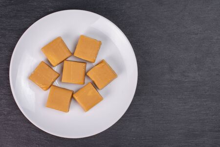Group of seven whole sweet golden caramel candy on white ceramic plate flatlay on grey stoneの写真素材
