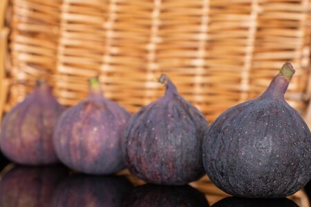 Group of four whole fresh fig fruit in row with braided rattan behindの写真素材