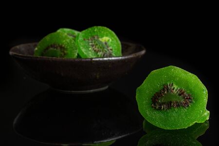 Group of four slices of sweet green candied kiwifruit in dark ceramic bowl isolated on black glassの写真素材