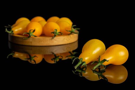 Lot of whole fresh yellow pear tomato on bamboo coaster isolated on black glassの写真素材