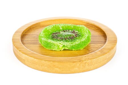 One slice of sweet green candied kiwifruit on bamboo coaster isolated on white backgroundの写真素材