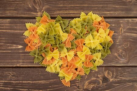 Lot of whole red, yellow and green uncooked farfalle flatlay on brown woodの写真素材