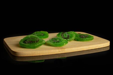 Group of five slices of sweet green candied kiwifruit on bamboo cutting board isolated on black glassの写真素材