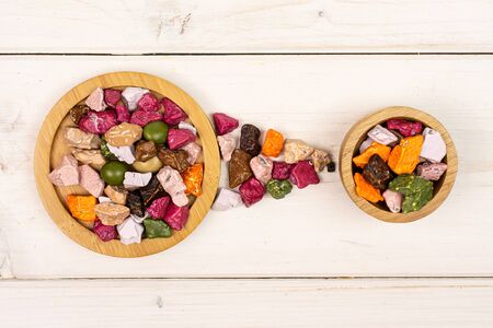 Lot of whole sweet chocolate stone on bamboo coaster in tiny wooden bowl flatlay on white woodの写真素材