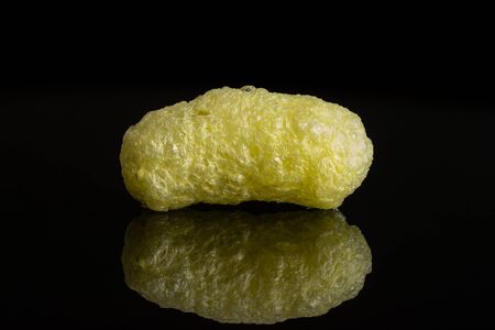 One whole salted yellow corn puff isolated on black glass
