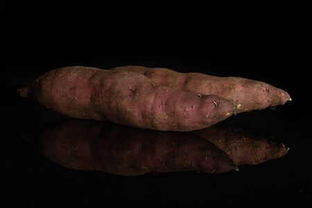 Group of two whole fresh brown sweet potato isolated on black glassの写真素材