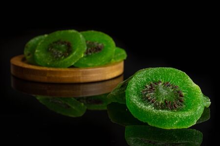 Group of four slices of sweet green candied kiwifruit on bamboo coaster isolated on black glassの写真素材