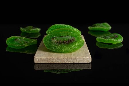 Group of seven slices of sweet green candied kiwifruit on small wooden cutting board isolated on black glassの写真素材