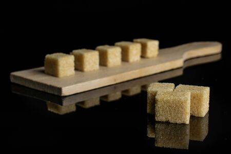 Group of eight whole sweet brown sugar cube on small wooden cutting board isolated on black glassの写真素材