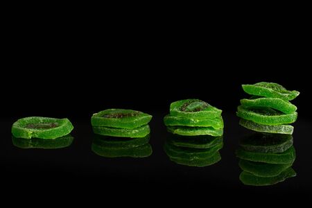 Group of ten slices of sweet green candied kiwifruit isolated on black glassの写真素材