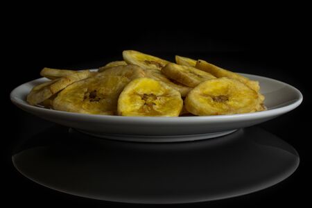 Lot of slices of sweet yellow dry banana on white ceramic plate isolated on black glassの写真素材