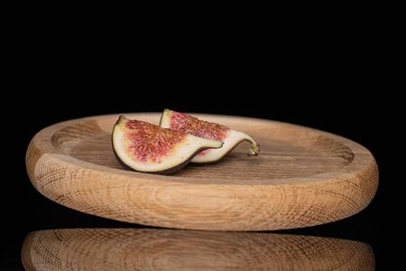 Group of two slices of fresh fig fruit on bamboo plate isolated on black glass
