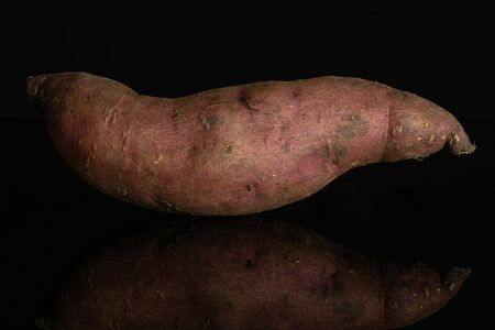 One whole fresh brown sweet potato isolated on black glassの写真素材