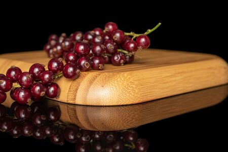 Lot of whole fresh dark redcurrant on wooden square plate isolated on black glass