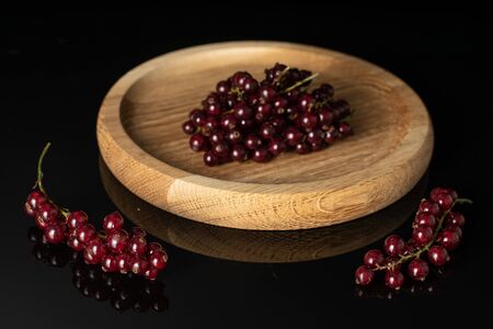Lot of whole fresh dark redcurrant on bamboo plate isolated on black glass