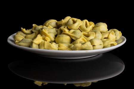 Lot of whole fresh yellow spinach filled tortelloni on white ceramic plate isolated on black glassの写真素材