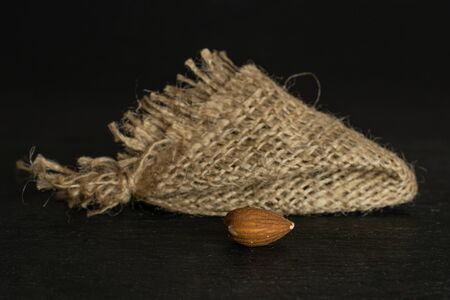One whole front focus brown almond nut with jute fabric isolated on grey stoneの写真素材