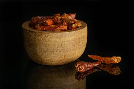 Lot of whole hot dry red chili pepper peperoncino in wooden bowl isolated on black glassの写真素材