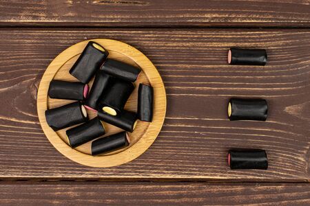Lot of whole sweet black liquorice candy on bamboo coaster flatlay on brown woodの写真素材