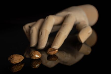 Group of three whole brown almond nut in row with wooden arm isolated on black glass