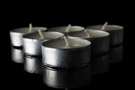Group of seven whole waxy white tea candle isolated on black glassの写真素材