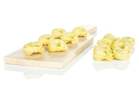 Lot of whole fresh yellow spinach filled tortelloni on small wooden cutting board isolated on white backgroundの写真素材