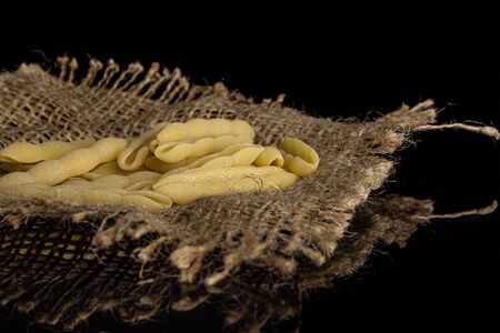 Lot of whole uncooked pasta cavatelli on jute cloth isolated on black glassの写真素材