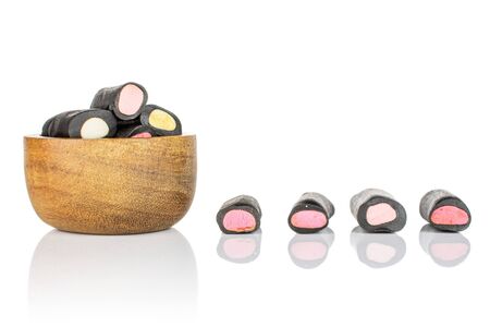 Lot of whole sweet black liquorice candy in tiny wooden bowl isolated on white backgroundの写真素材