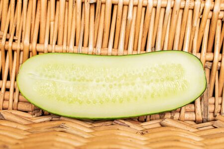 One half of fresh green pickling cucumber with braided rattan behind