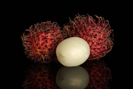 Group of three whole fresh red rambutan one peeled isolated on black glassの写真素材