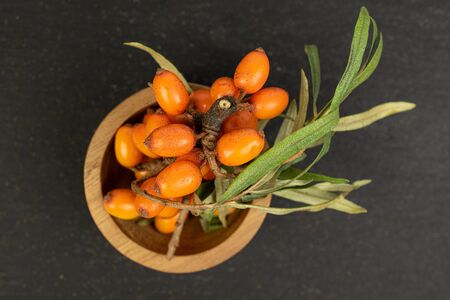 Lot of whole fresh ripe orange sea buckthorn berry in bamboo bowl flatlay on grey stoneの写真素材