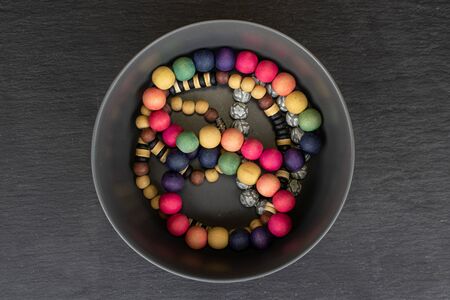 Lot of whole wooden bead in small ceramic bowl flatlay on grey stone
