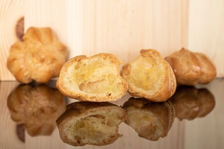 Group of two whole two halves of baked golden profiterole on glass with natural wood behind