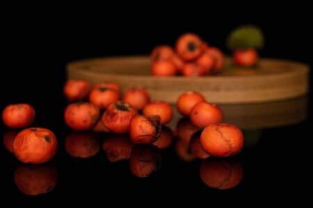 Lot of whole wild orange rowanberry on round bamboo coaster isolated on black glassの写真素材