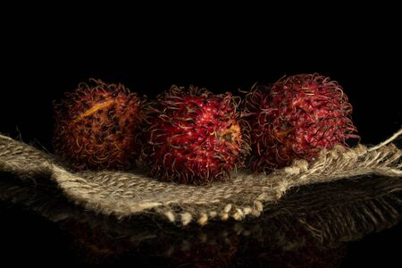 Group of three whole fresh red rambutan on jute cloth isolated on black glassの写真素材