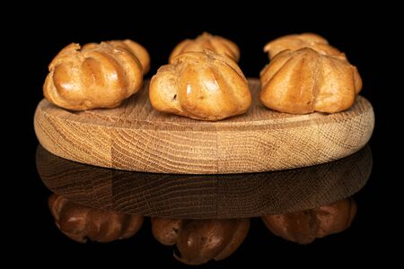 Group of three whole fresh baked golden profiterole on bamboo plate isolated on black glass