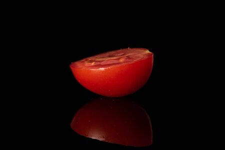 One half of fresh red tomato isolated on black glassの写真素材