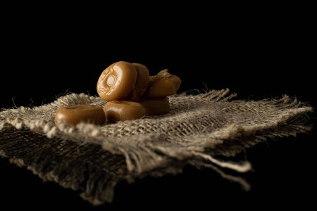 Lot of whole caramel brown candy with jute fabric isolated on black glassの写真素材