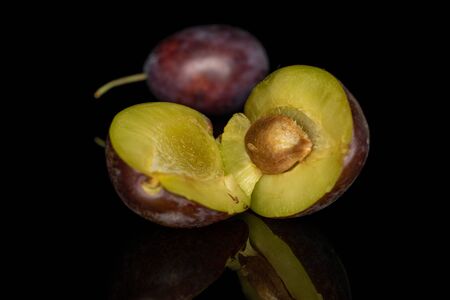 Group of one whole two halves of sweet purple plum isolated on black glass