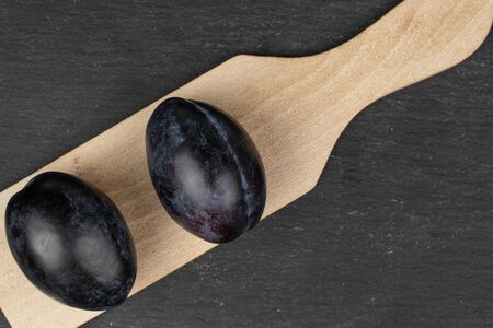 Group of two whole fresh purple plum on wooden cutting board flatlay on grey stoneの写真素材