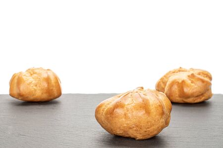 Group of three whole baked golden profiterole on grey stone isolated on white background