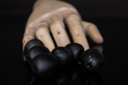 Group of six whole tasty black olive with wooden hand isolated on black glass