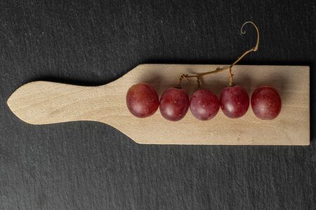 Group of five whole fresh purple grape rose on wooden cutting board flatlay on grey stone