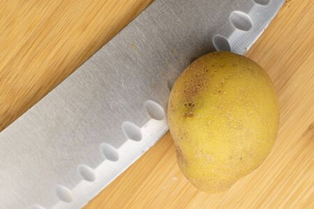 One whole raw brown potato with steel knife flatlay on light wood