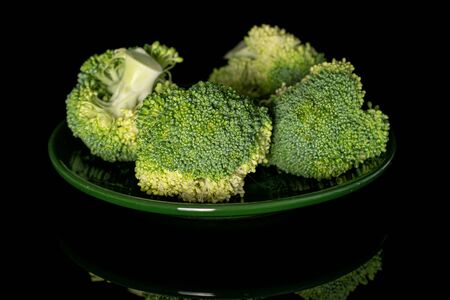 Group of four whole fresh green broccoli on green plate isolated on black glassの写真素材