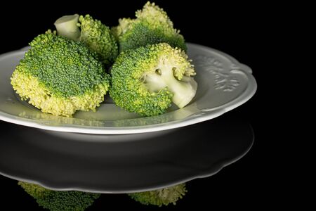 Group of four whole fresh green broccoli on white plate isolated on black glass