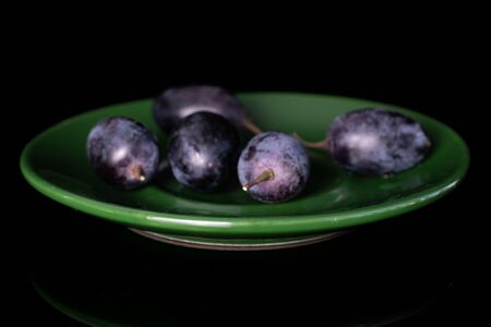 Group of five whole fresh black grape on green plate isolated on black glassの写真素材