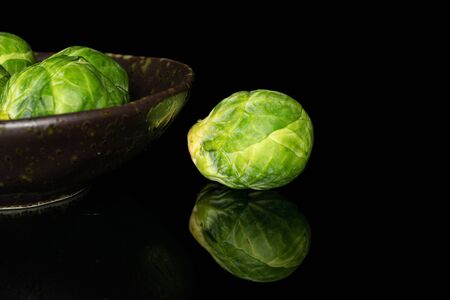 Group of three whole fresh green brussels sprout on glazed bowl isolated on black glassの写真素材