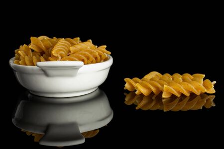 Lot of whole dry brown wholegrain fusilli in white oval ceramic bowl isolated on black glassの写真素材